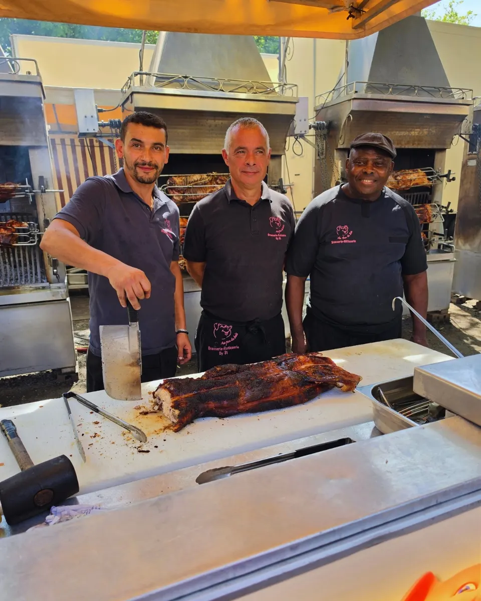 Deux rôtisseurs présentent fièrement un cochon entier rôti à la broche